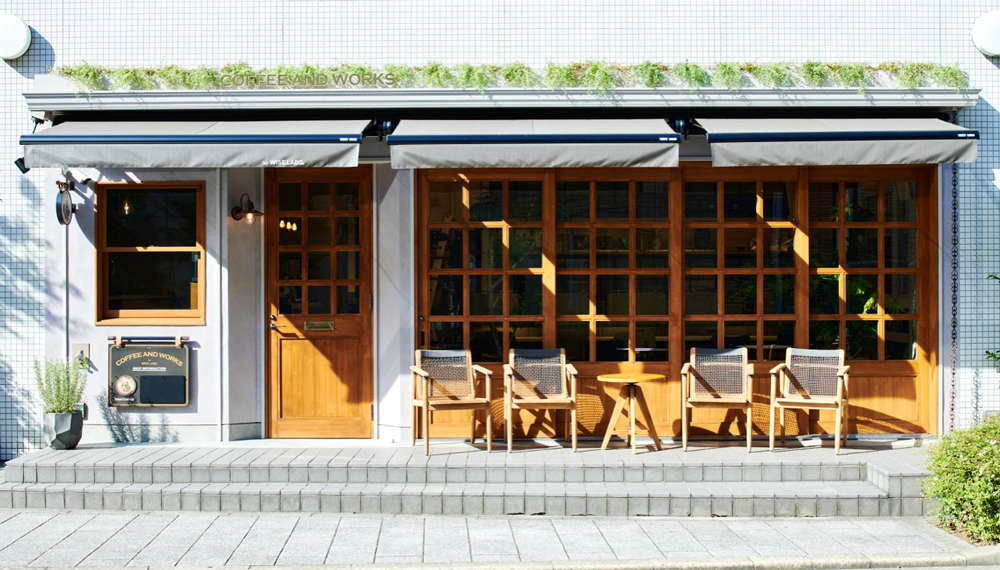 COFFEE AND WORKSのカフェ外観。木製テラス席と白いオーニング、明るい日差しに包まれた開放的な空間