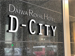 黒い石目調の壁面に白い文字で「DAIWA ROYAL HOTEL D-CITY」と刻まれたホテルサイン