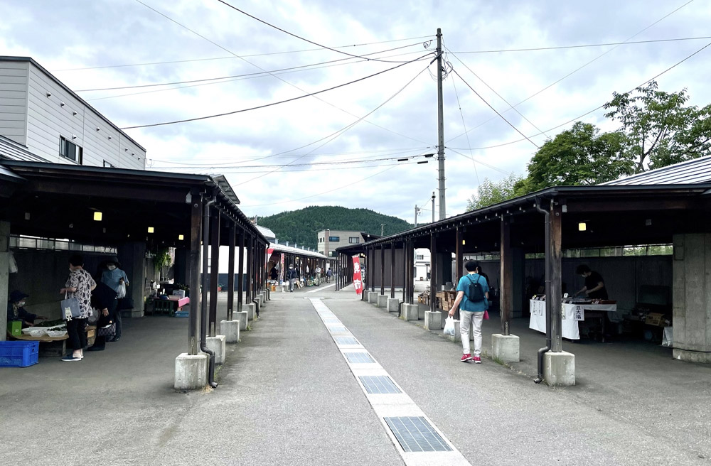 緑の山を背景に両側に屋根付きの出店が並ぶ朝市の様子
